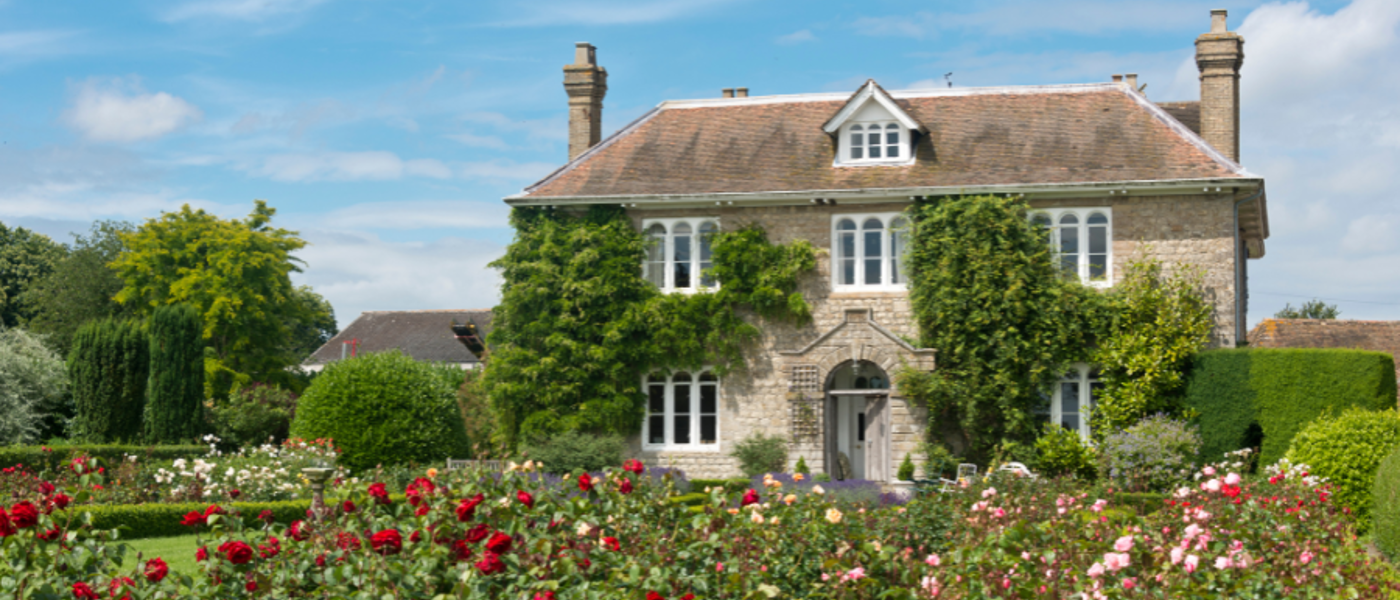 Large country house with a rose garden in the foreground on a sunny day