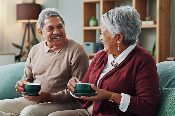 Senior Couple On A Sofa Smiling at each other Holding Cups And Saucer in their hands