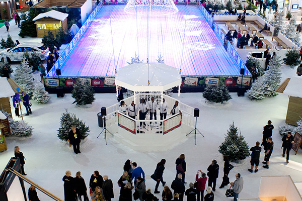 an ice Rink in the Ideal Home Exhibition hall, surrounded by imitation Snow and Chalets