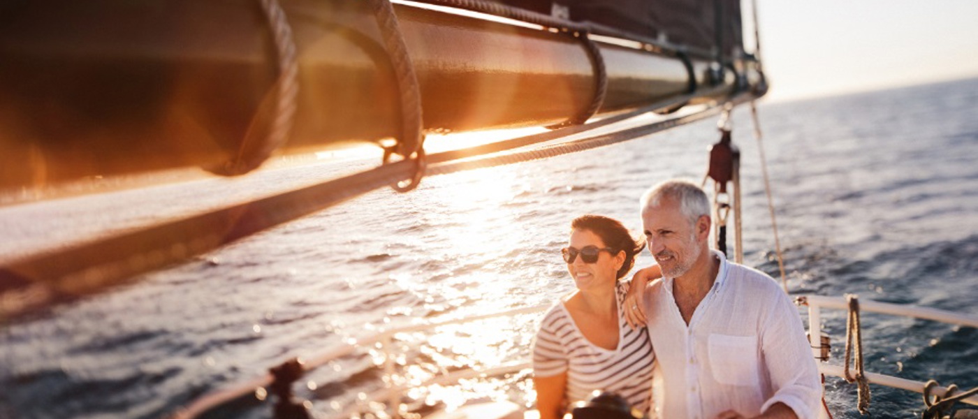 Middle aged couple standing on the deck of a sailing boat at sea