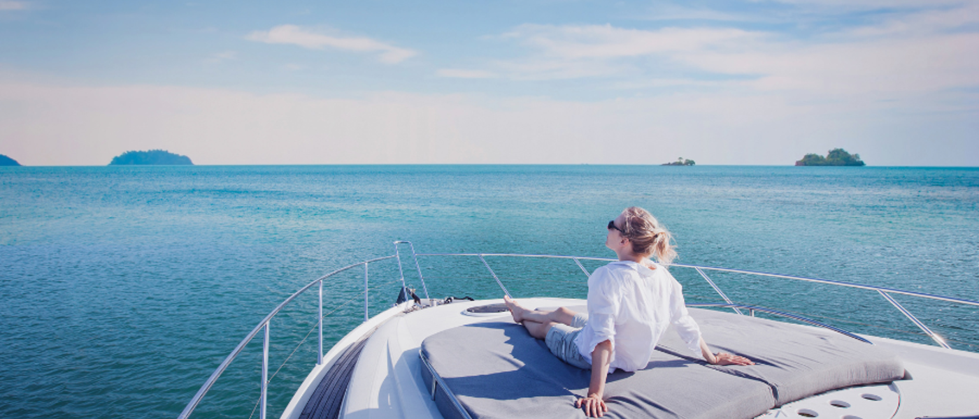 Woman in a white shirt sitting in the sun on the deck of a yacht at sea