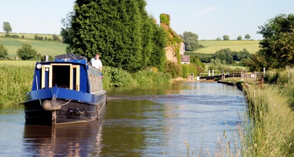 Man standing on a blue narrowboat on a canal in the sunshine