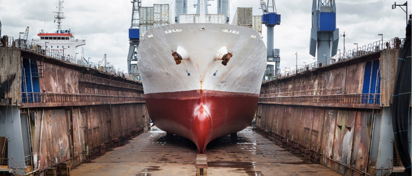 Front view of a white cargo ship with a red hull in a dry dock