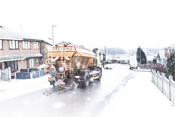 A yellow snow gritter on a snowy residential street