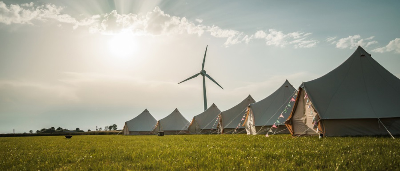 Glamping tents on a grassy field with a wind turbine behind them