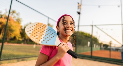Close up of young girl smiling with a tennis racket against one shoulder on a tennis court