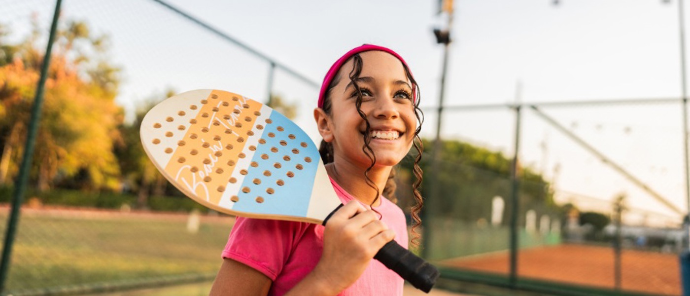 Close up of young girl smiling with a tennis racket against one shoulder on a tennis court