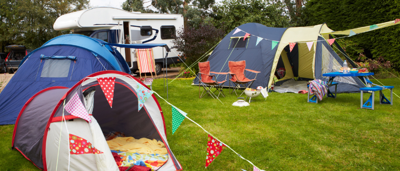 3 colourful tents with bunting outside on green grass with a caravan in the background